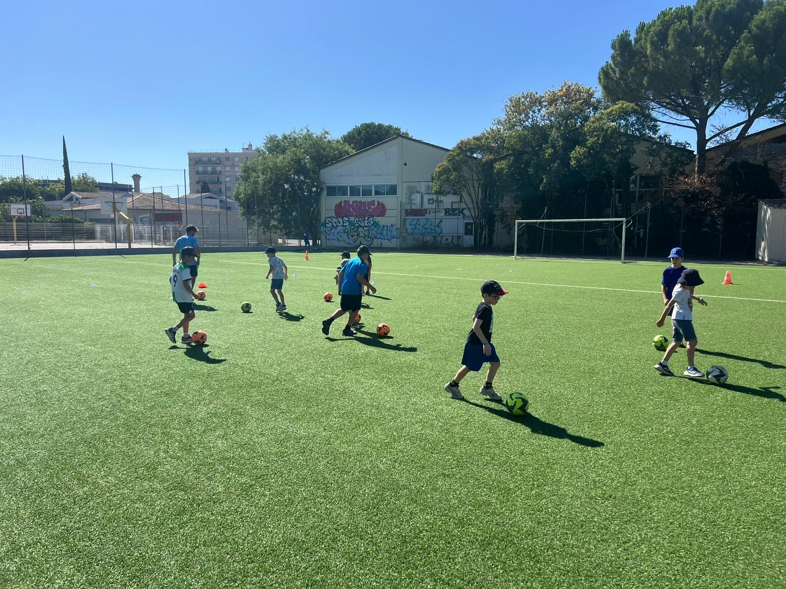 Enfants jouent au football sur un terrain ensoleillé.