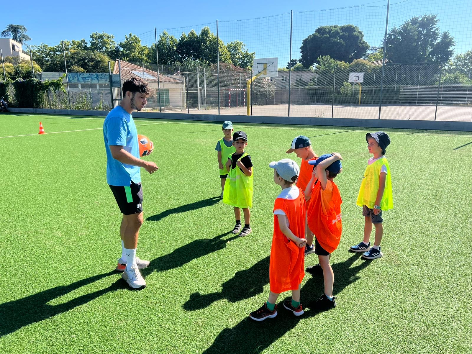 Entraîneur de football animateur avec enfants sur terrain gazonné.