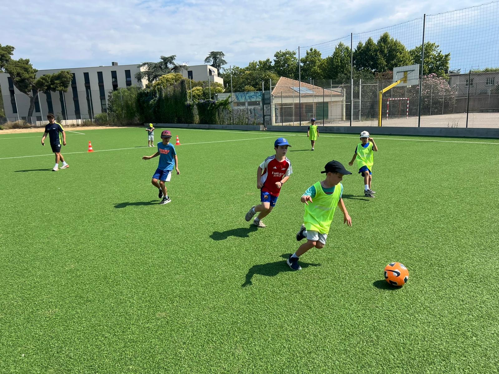 Enfants jouant au football sur un terrain ensoleillé.