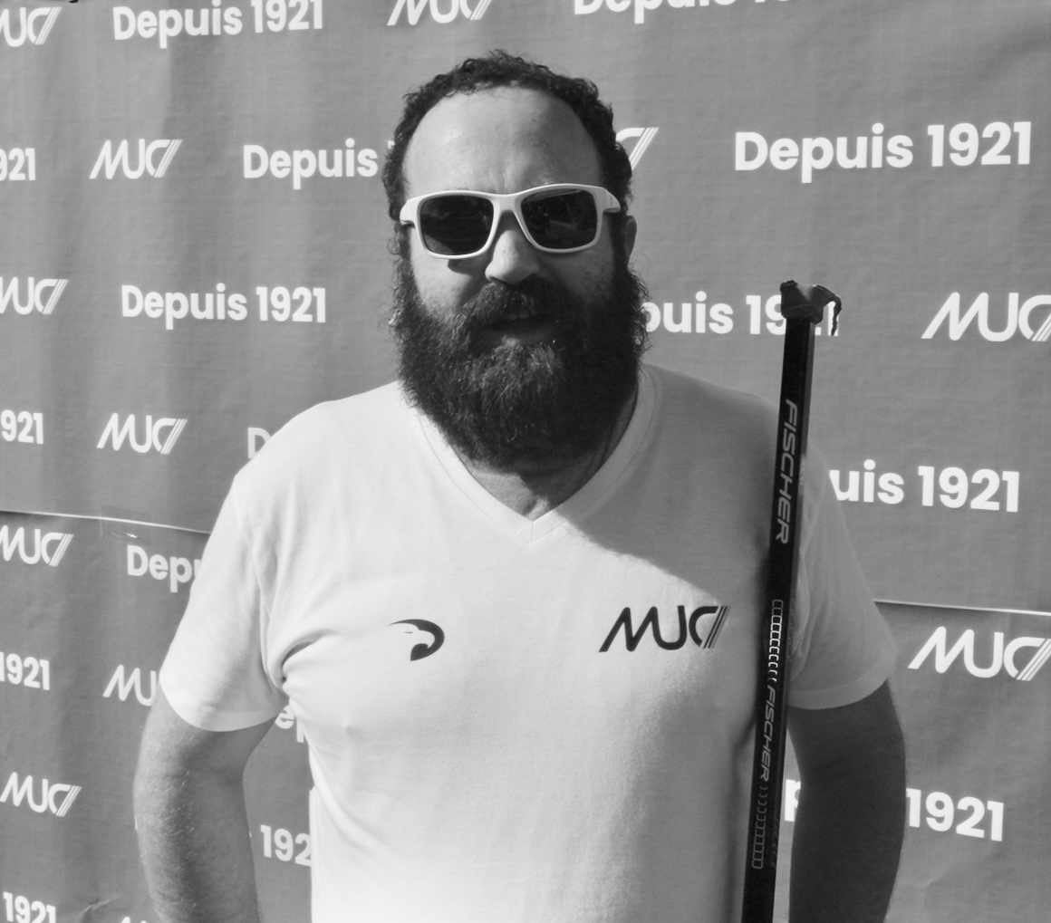 Homme barbu, T-shirt MUC, lunettes de soleil blanches.