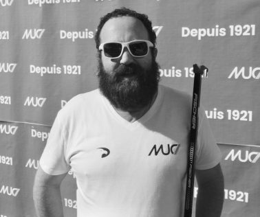 Homme barbu, T-shirt MUC, lunettes de soleil blanches.